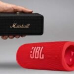 a hand holding a speaker next to a red speaker, jbl vs marshall comparison