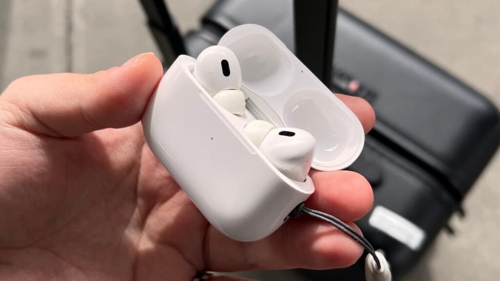 a hand holding a white case with two white earbuds apple