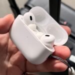 a hand holding a white case with two white earbuds apple