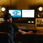 Man in Black Shirt Wearing Headphones in Front of Monitors